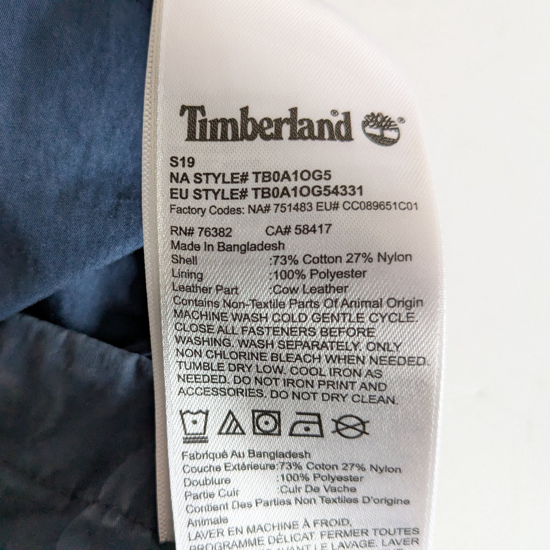 Close-up of a Timberland garment care label sewn onto blue denim fabric, showing product details and care instructions.