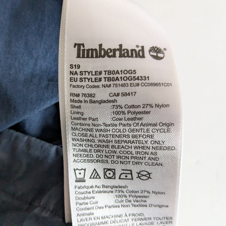 Close-up of a Timberland garment care label sewn onto blue denim fabric, showing product details and care instructions.
